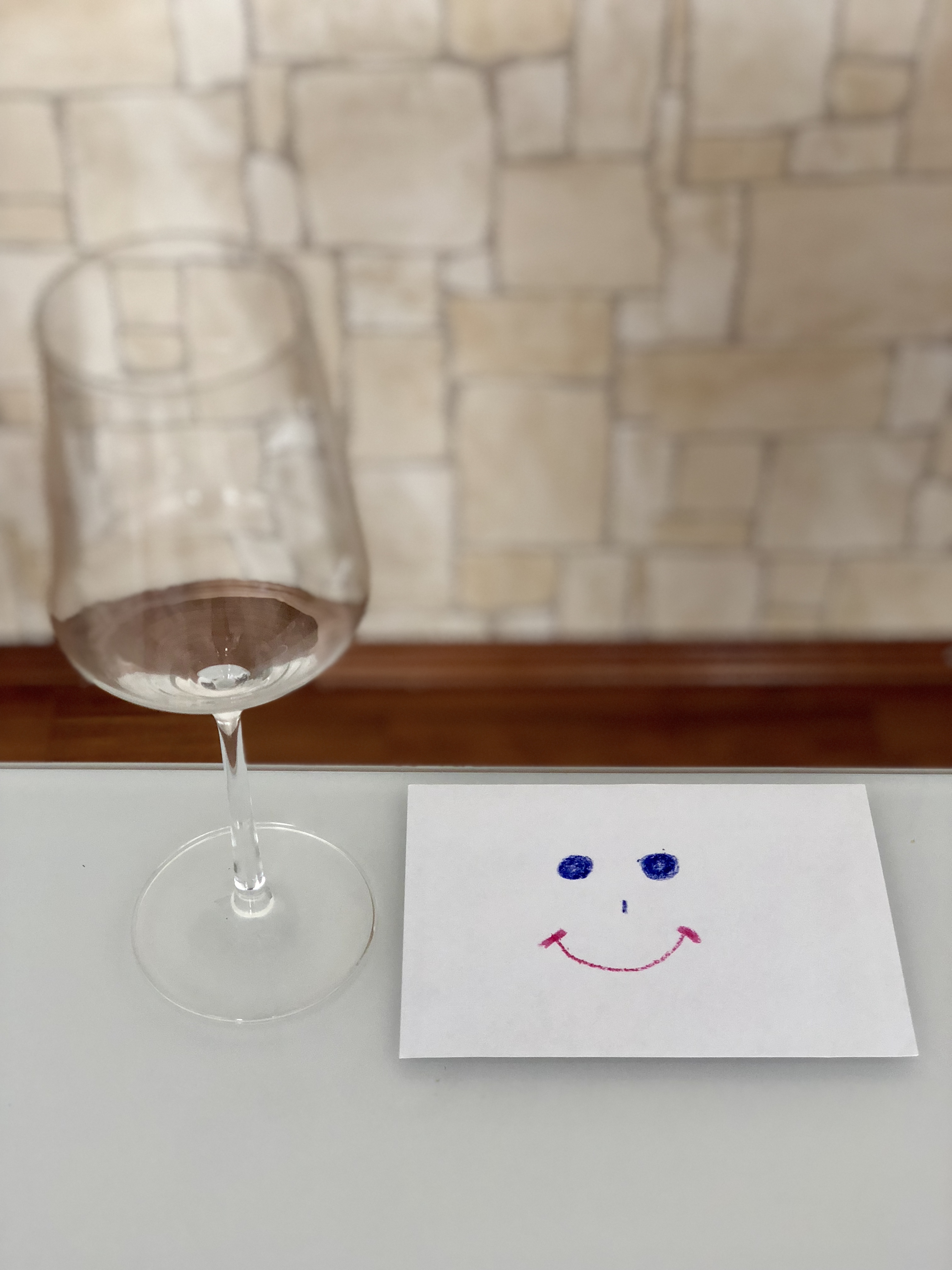Ein leeres Weinglas am Tisch neben einem Smiley am Papier