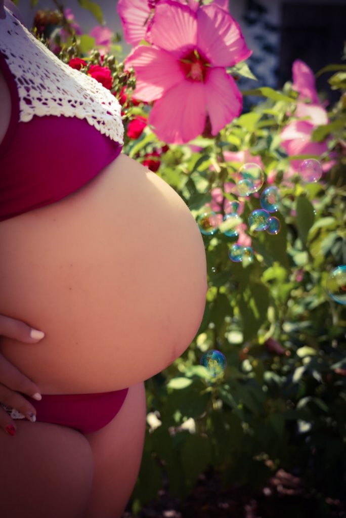 Mein Babybauch im Sonnenschein vor Blumen