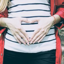 Frau formt mit den Händen ein Herz über dem Babybauch