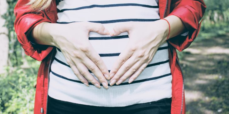 Frau formt mit den Händen ein Herz über dem Babybauch