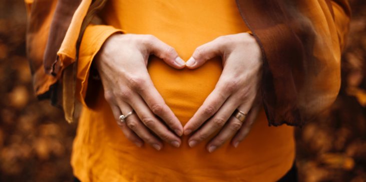 Hände auf dem Bauch einer werdenden Mutter, die ein Herz formen.