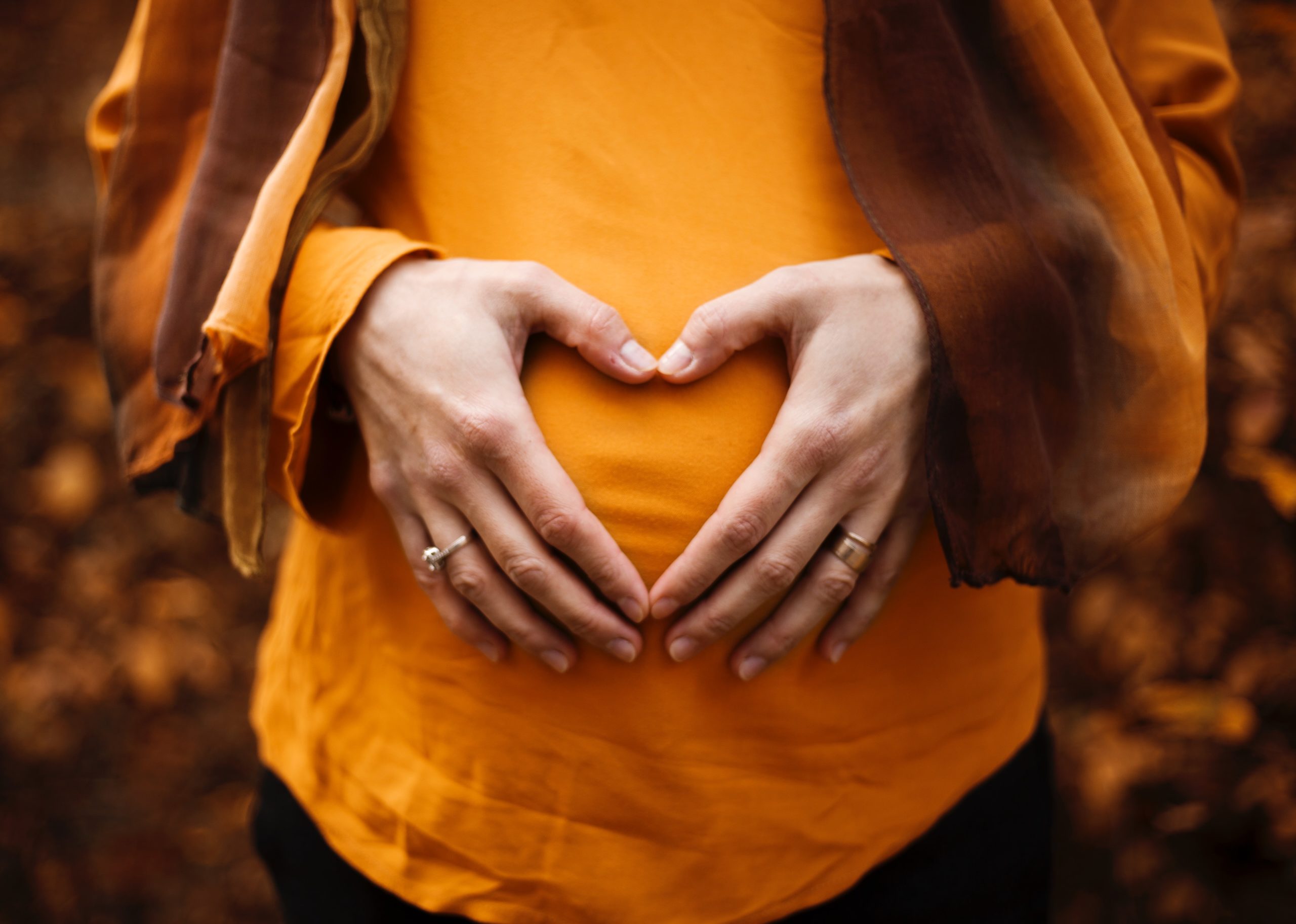 Hände auf dem Bauch einer werdenden Mutter, die ein Herz formen.