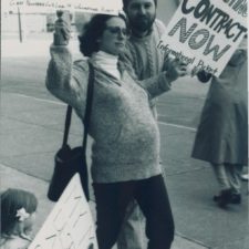 Eine schwangere Frau auf einer Demonstration hält Protestschilder hoch aus dem Jahr 1990