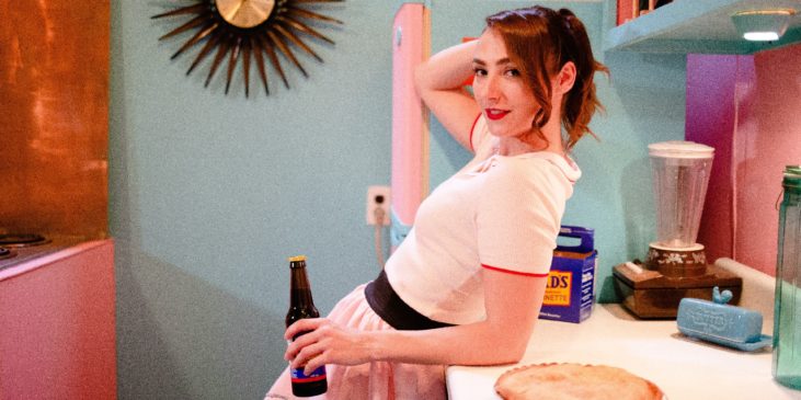 eine schöne Frau lehnt am Küchentisch mit einer Flasche Bier in der Hand - Werbung für Alkohol