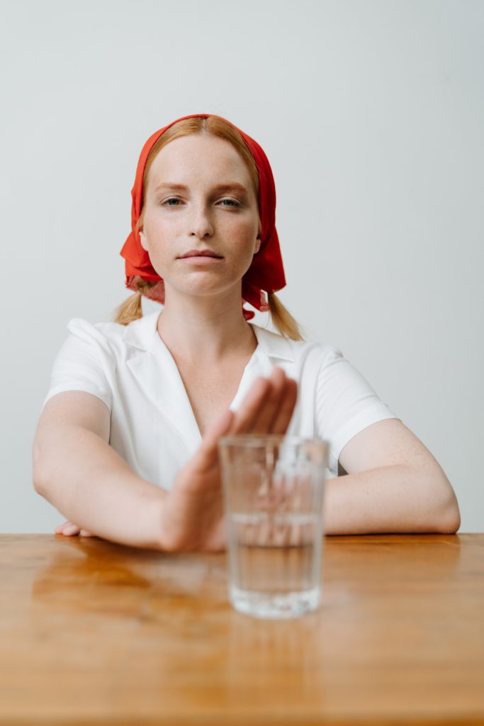 Ein Frau mit Kopftuch sitzt am Tisch und hält die Hand vor ein Glas Alkohol