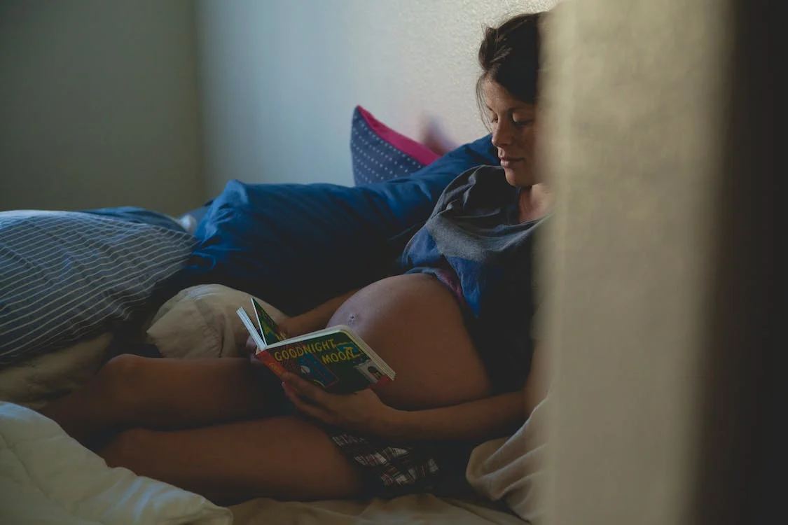 Schwangere Frau liegt im Bett und liest