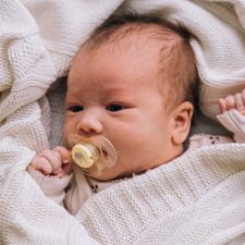 Ein Baby liegt in eine Decke eingewickelt und mit einem Schnuller im Mund