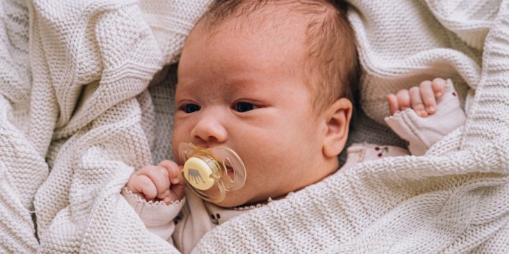 Ein Baby liegt in eine Decke eingewickelt und mit einem Schnuller im Mund