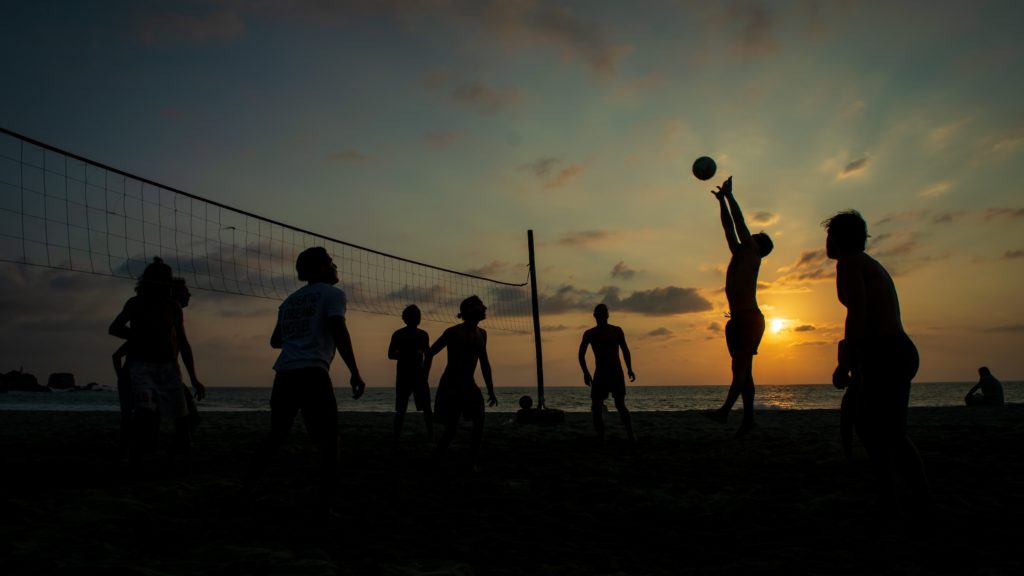 Gesunde sportliche Menschen die keinen Alkohol trinken spielen im Sonnenuntergang am Strand beachvollyball