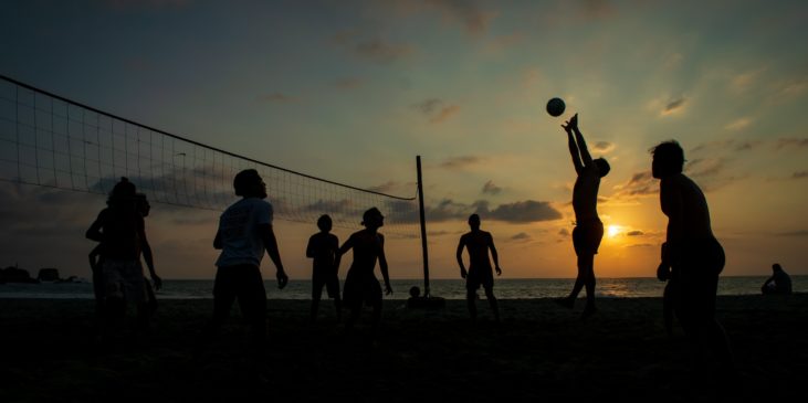 Gesunde sportliche Menschen die keinen Alkohol trinken spielen im Sonnenuntergang am Strand beachvollyball